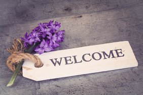 Auf dem Bild zu sehen: Ein "Welcome-Schild" samt Blume für das symbolische "Willkommen" auf der neuen NÖ ARGE für Pflege und Betreuung-Website; 