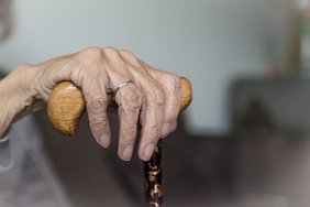 Am Bild zu sehen eine Hand einer älteren Person, die fest einen Gehstock umklammert; 